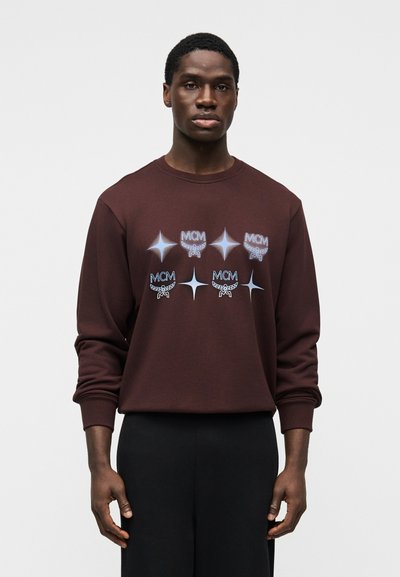 Sweat-shirt en coton marron avec grands logos MCM blancs et bleus ainsi que des motifs d'étoiles sur le devant. Poignets et encolure côtelés, coupe décontractée.