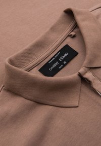 Hnědá polo tričko s ribbovaným límcem, s visačkou "OMBRA EXIMMO" a velikostí "M." Hladká textura a neformální design.