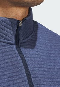 Dunkelblaue Jacke mit Reißverschluss und strukturiertem Rippenmuster. Verfügt über einen hohen Kragen und einen glatten Reißverschluss. Der Stoff wirkt weich und leicht.