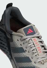Szare buty sportowe z teksturowaną górą, ciemnoszarymi akcentami i czerwonym logotypem. Charakteryzują się mocnymi sznurowadłami i wzorzystą podeszwą.