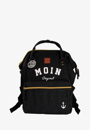 Black denim backpack with yellow zipper, white lettering "MOIN Original," anchor design, and brown leather patch. Two front pockets.