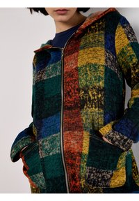 Bunte Kapuzenjacke mit einem karierten Muster in Grün, Rot, Blau und Gelb. Das Material ist ein strukturierter Strickstoff mit einem frontalen Reißverschluss.