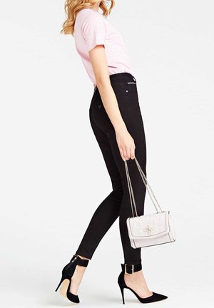 Sorte skinny jeans med høj talje, kombineret med en pink t-shirt. Tilbehør inkluderer en hvid håndtaske og sorte højhælede sko.