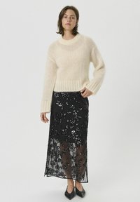 Kremasto obarvan, puhast pulover z rebrastim spodnjim robom, kombiniran s črno, bleščečo, prosojno maxi krilo z rožnatimi vzorci. Črne koničaste balerinke.