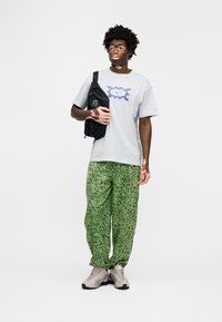 Γκρι μπλουζάκι με μοβ γραφικό σχέδιο, σε συνδυασμό με πράσινο παντελόνι με σχέδια. Η εμφάνιση ολοκληρώνεται με γκρι αθλητικά παπούτσια και μαύρη τσάντα.