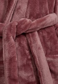 Accappatoio morbido e soffice in un tenue color malva, con vita legata, colletto a risvolto e due tasche anteriori dalla texture pelosa.