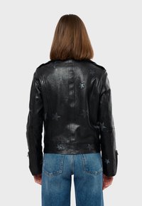 Crna kožna jakna s uzorcima zvijezda, koja ima uski kroj i glatku teksturu. Uključuje patentne zatvarače na rukavima i ramene epaulete.