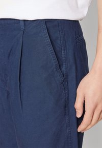 Námořnické modré kalhoty s jemnou texturou, bočními kapsami a decentními sklady vpředu, které zdůrazňují přiléhavý střih a praktický design.