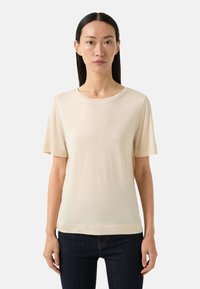 Cremefarvet t-shirt med korte ærmer, rund halsudskæring, glat tekstur og afslappet pasform. Bæret med mørkeblå jeans.