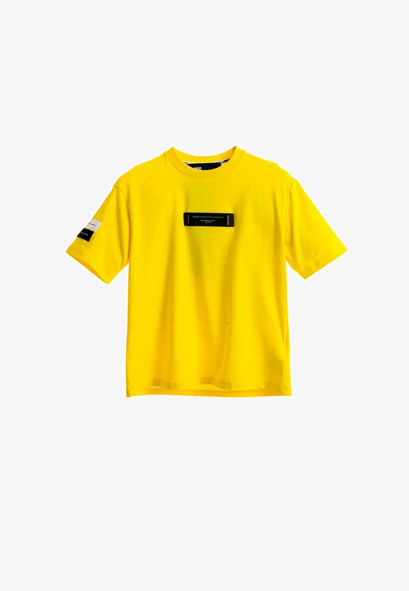 Camiseta amarilla de algodón con mangas cortas, con una etiqueta rectangular negra en la parte delantera y dos etiquetas de acento en las mangas.