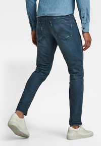 Džínové kalhoty v tmavě modrém leštění se slim fit střihem, s zadními kapsami a jemnými detaily opotřebení, spárované s bílými teniskami.