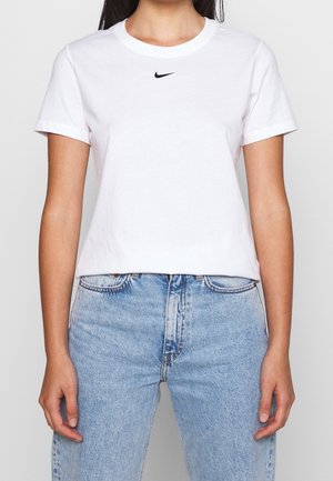 Biała bawełniana koszulka z okrągłym dekoltem i krótkimi rękawami, z małym czarnym logo Nike na piersi. Połączona z jasnoniebieskimi dżinsami.