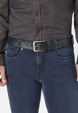 Black textured belt with a silver buckle worn over blue denim jeans. The shirt is dark, long-sleeved with buttons.