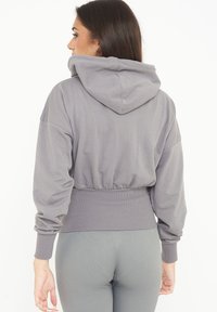Felpa grigia corta con cappuccio regolabile, vita elastica e polsini a coste. Tessuto morbido con maniche lunghe e vestibilità rilassata.