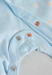 Vêtement pour bébé bleu clair avec boutons-pression en argent et cuivre, orné de petits motifs de marguerites blanches et jaunes.