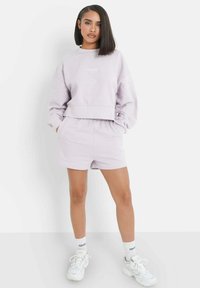 Ljuslila sweatshirt med kortad design och ribbade ärmmuddar, tillsammans med matchande shorts. Vita träningsskor och strumpor med logotypdetaljer.