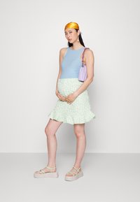 Top sem mangas azul claro, saia ruffled floral verde menta, sandálias de plataforma bege com tiras verdes, mala roxa, acessório de lenço dourado.