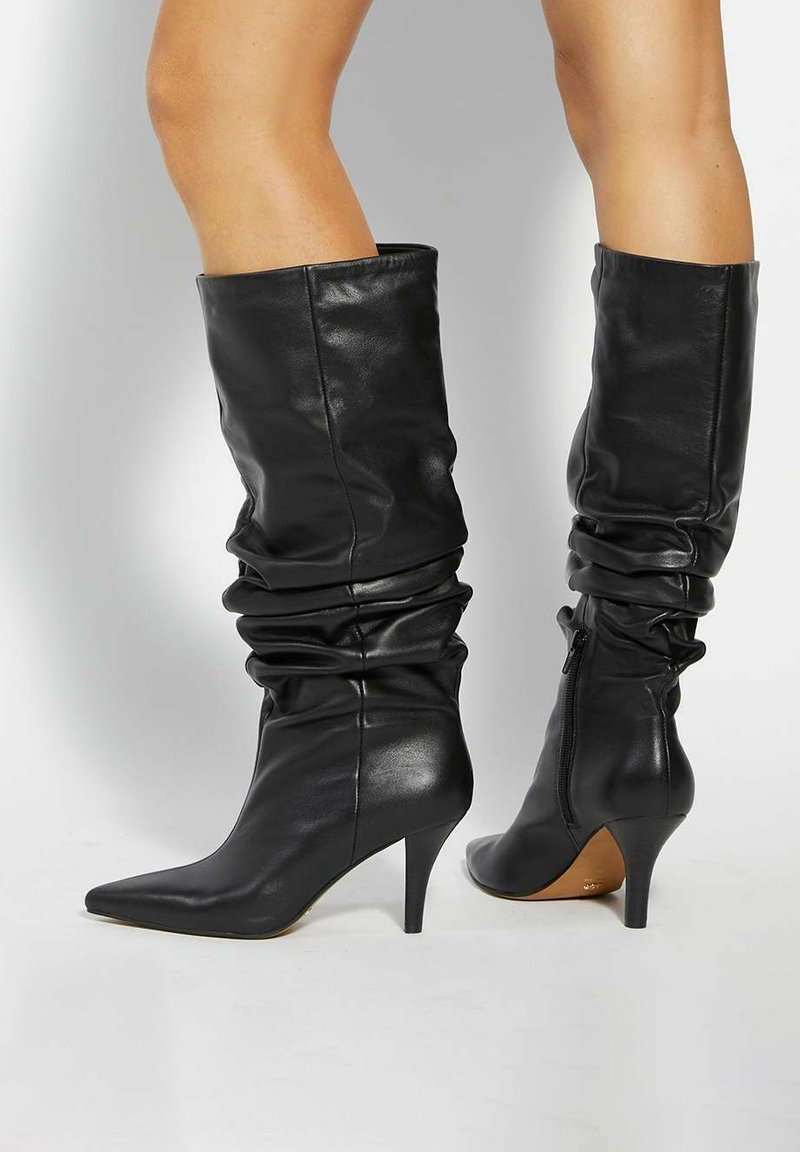 Black leather knee-high boots with a slouchy design, pointed toe, and a stiletto heel. Zipper closure on the side. Smooth texture.