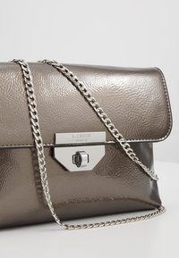 Metallic grå taske med en tekstureret overflade, der har en kædledel og en sølvfarvet spænde med logodetaljer.