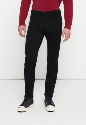 Hombre vistiendo vaqueros negros de corte ajustado, un jersey rojo de manga larga y zapatillas negras altas con suelas blancas y punteras blancas.