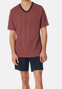 Rot und marinefarbenes kurzärmeliges V-Ausschnitt-T-Shirt mit geometrischem Muster, ausgestattet mit einer Brusttasche und kombiniert mit marinefarbenen Shorts. Weicher Stoff.