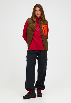Isolierte Olivenweste mit orangener Tasche, rotem Reißverschlussoberteil und dunkler Cargo-Hose. Schwarze Stiefel mit roten Schnürsenkeln. Glatte Texturen und funktionales Design.