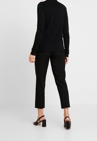 Svart långärmad tröja med rund hals, tillsammans med svarta raka byxor och svarta klacksandaler med remmar. Slät textur.