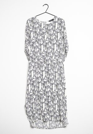 Robe blanche jusqu'aux genoux avec manches longues froncées, présentant un imprimé zèbre noir et blanc sur toute la surface, suspendue sur un cintre noir.