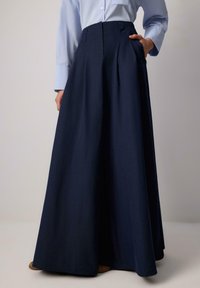 Marineblauer, langer Rock mit Falten aus leichtem Stoff, mit seitlichen Taschen und hohem Taillenbund. Glatte Textur und eleganter Fall.