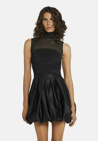 Robe noire avec un corsage ajusté et un décolleté transparent, une taille froncée et une jupe volumineuse et texturée. Tissu lisse avec un doux éclat.
