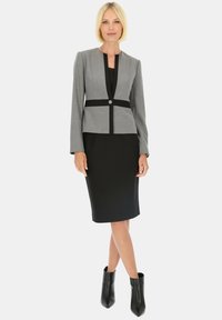 Szary dopasowany żakiet z czarnymi akcentami, zapinany na jeden guzik, w zestawieniu z czarną dopasowaną sukienką i czarnymi botkami za kostkę. Gładkie materiały w całej stylizacji.