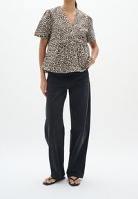 Top a stampa leopardata con maniche corte, scollatura a V e design peplum, abbinato a jeans neri a vita alta e gamba larga e infradito neri.
