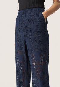 Navyblauwe kanten broek met een geometrisch patroon, voorzien van een elastische tailleband en zijzakken. Textuurstof met uitsnijdingen.