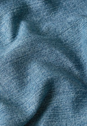 Primer plano de tela vaquera azul texturizada que muestra hilos tejidos y suaves pliegues que crean sombras tenues.