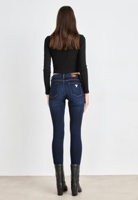 Tmavomodré úzke džínsy s vysokým pásom, so spodnými dvoma vreckami a trojuholníkovou nášivkou. Nosí sa s čiernym dlhým rukávom a čiernymi čižmami.