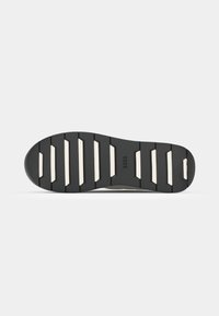 Semelle de chaussure en caoutchouc noir avec des accents blancs, présentant un motif nervuré et un bout légèrement arrondi. Logo "BOSS" embossé sur la surface.