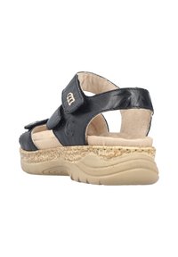 Sandale en cuir noir avec des sangles ajustables, semelle intérieure rembourrée beigne, et semelle extérieure texturée beige, avec un accent décoratif sur le côté.