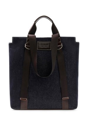 Bolsa tote de tela azul oscuro con dos asas marrones y etiqueta frontal cosida con el nombre de la marca Guess Est. 1981.