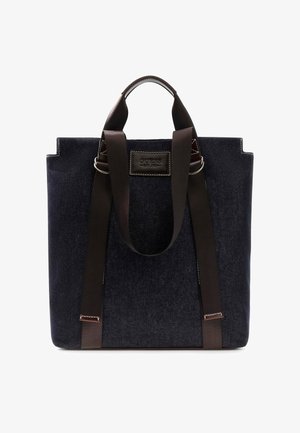 Bolsa tote de tela azul oscuro con dos asas marrones y etiqueta frontal cosida con el nombre de la marca Guess Est. 1981.