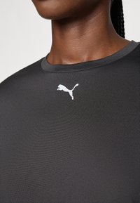 T-shirt de sport noir en tissu lisse, avec un col rond et un logo Puma blanc sur le côté gauche de la poitrine.