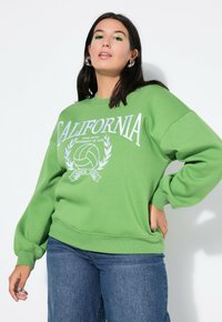 Zelená fleecová mikina s nápisem "CALIFORNIA" a grafikou volejbalu. Pohodlný střih s žebrovanými manžetami a lemem, nošena s džíny.