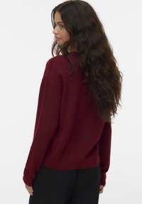 Übergroßer burgunderfarbener Pullover mit strukturiertem Strick, gerippten Bündchen und abgerundetem Saum, kombiniert mit schwarzen Hosen.