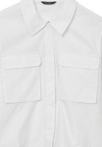 Camicia bianca con bottoni realizzata in tessuto liscio, dotata di un colletto a punta e due tasche sul petto con pattina. Design semplice e pulito.