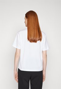 Weißes Baumwoll-T-Shirt mit kurzen Ärmeln, Rundhalsausschnitt und lockerer Passform, von hinten betrachtet. Weiche Textur und minimalistisches Design.