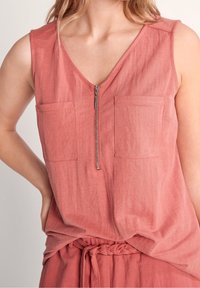Débardeur rose sans manches avec un col en V, une fermeture éclair à l'avant et deux poches plaquées sur la poitrine. Fabriqué en tissu léger avec une finition texturée.