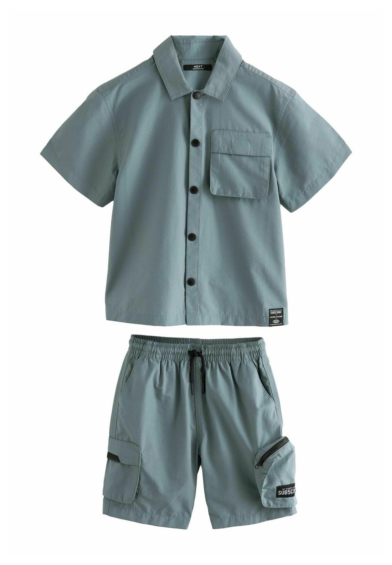 Chemise légère verte à manches courtes avec fermeture à boutons et poche, associée à un short assorti avec une taille élastique et une poche latérale.