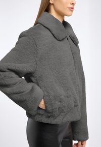 Szara kurtka z sztucznego futra, krótka, z szerokim kołnierzem, kieszeniami po bokach i miękką teksturą; zaprojektowana z długimi rękawami i zapięciem na guziki.