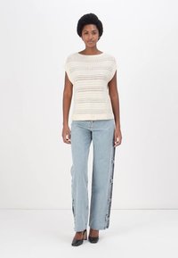 Krēmveida adīta blūze ar īsām piedurknēm un atvērta šuvuma rakstu, apvienota ar gaiši ziliem taisnām kājām džinsiem ar sānu paneļu detaļām. Melnas kurpes ar papēžiem.