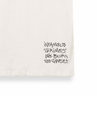 Camiseta de algodón blanca con un texto en estilo graffiti negro en la parte inferior izquierda, mostrando varias frases en un diseño superpuesto.