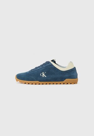 Mėlyni suede sportbačiai su balta liežuvėlio ir kulno akcentais, apvalus guminis padas su sukibimu ir išsiuvinėtas 'cK' logotipas šone.